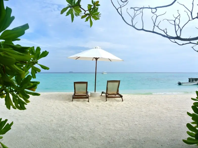 Two loungers under a white umbrella on a white-sand beach by turquoise water